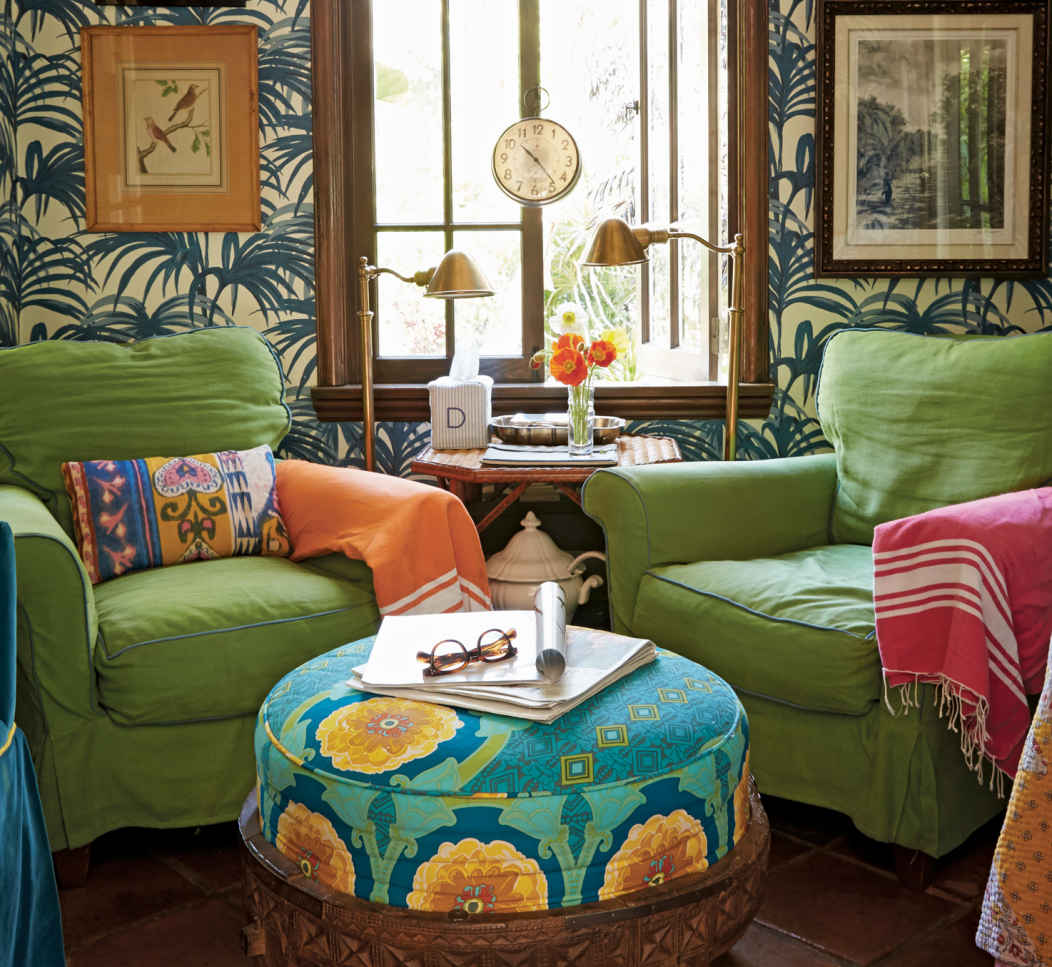KICK YOUR FEET UP. Offering a view into the busy kitchen, this lovely small sitting room—with its cozy green armchairs, tropical print ottoman, and palm frond wallpaper—is a welcome retreat while waiting for the oven timer to ding.