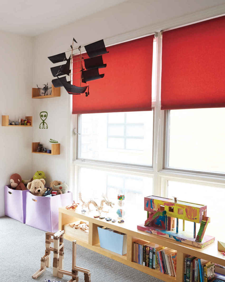 COLOR BLOCKING. White walls in a kids’ room make sense; their “stuff” is pretty vibrant. But adding some solid swipes of color on top—like these red blinds and purple toy bins—keeps things fun.